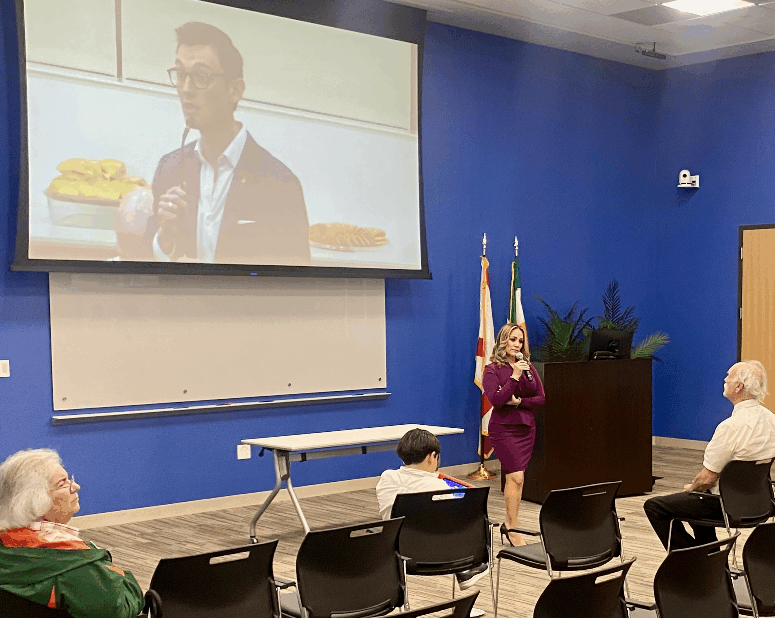 Commissioner Melissa Castro speaks to attendees at her town hall while a live feed projects Nicholas Cabrera from the audience asking a question. Cabrera pressed Castro on her proposed phased tax cut.