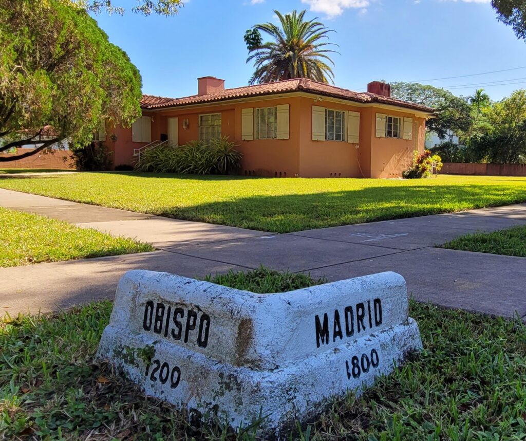 A single-story Mediterranean Revival–style house at 1258 Obispo Avenue in Coral Gables, with stucco walls, a red tile roof, and a corner street marker in the foreground. The home is the subject of a pending demolition appeal before the City Commission.