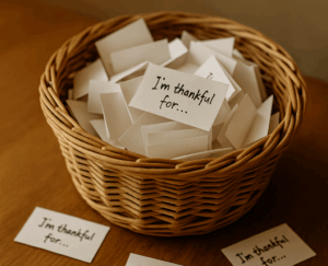 A woven basket sits on a wooden table filled with small folded cards labeled “I’m thankful for…,” with several slips spread around it.
