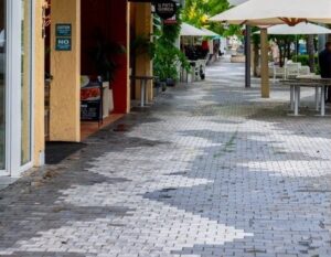 Paved sidewalk along Miracle Mile with storefront awnings, outdoor seating, and trees.