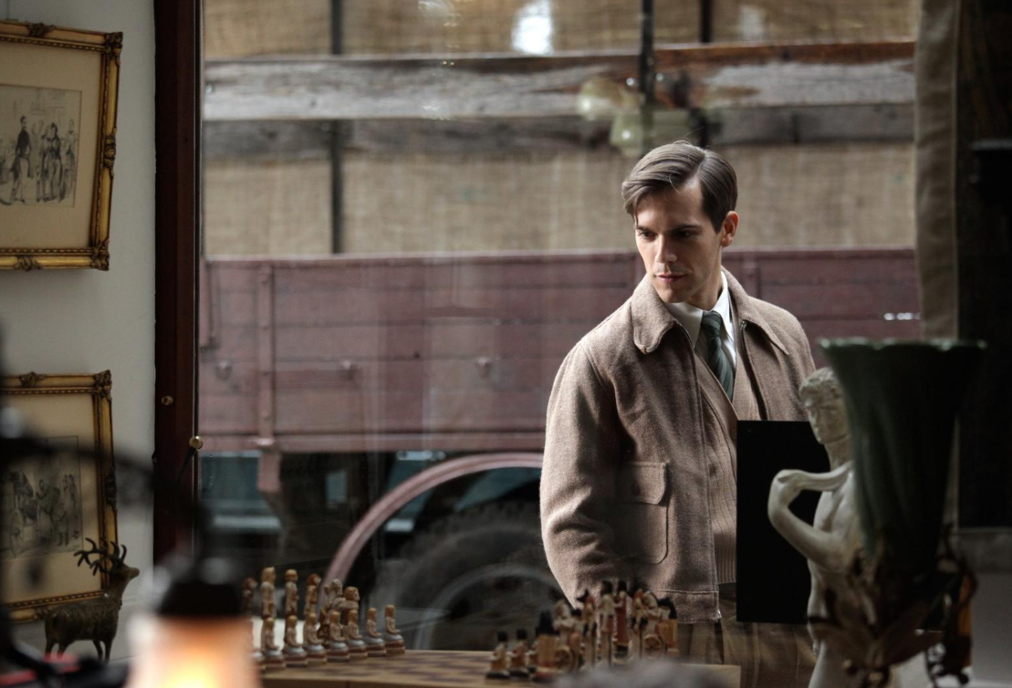 A man in a 1930s-era coat looks at a chess set through a shop window in a scene from the film The Chess Player.