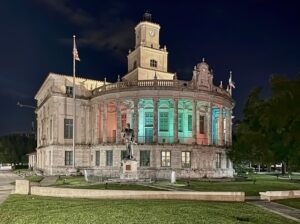 Exterior view of Coral Gables City Hall at dusk, with the historic Mediterranean Revival building illuminated against the evening sky, representing municipal governance and civic decision-making.
