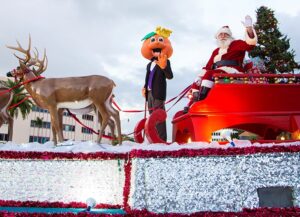 Santa Claus and the Junior Orange Bowl mascot ride a festive float with reindeer during the 2015 parade on Miracle Mile, reflecting the long-standing holiday tradition embraced by the Coral Gables community.