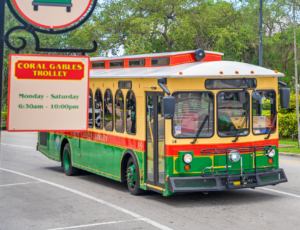 Coral Gables trolley bus traveling past a trolley stop sign along a city street.