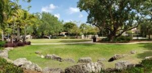 A wide green lawn bordered by trees and stone features in a Coral Gables neighborhood park, illustrating the city’s multi-use public spaces.