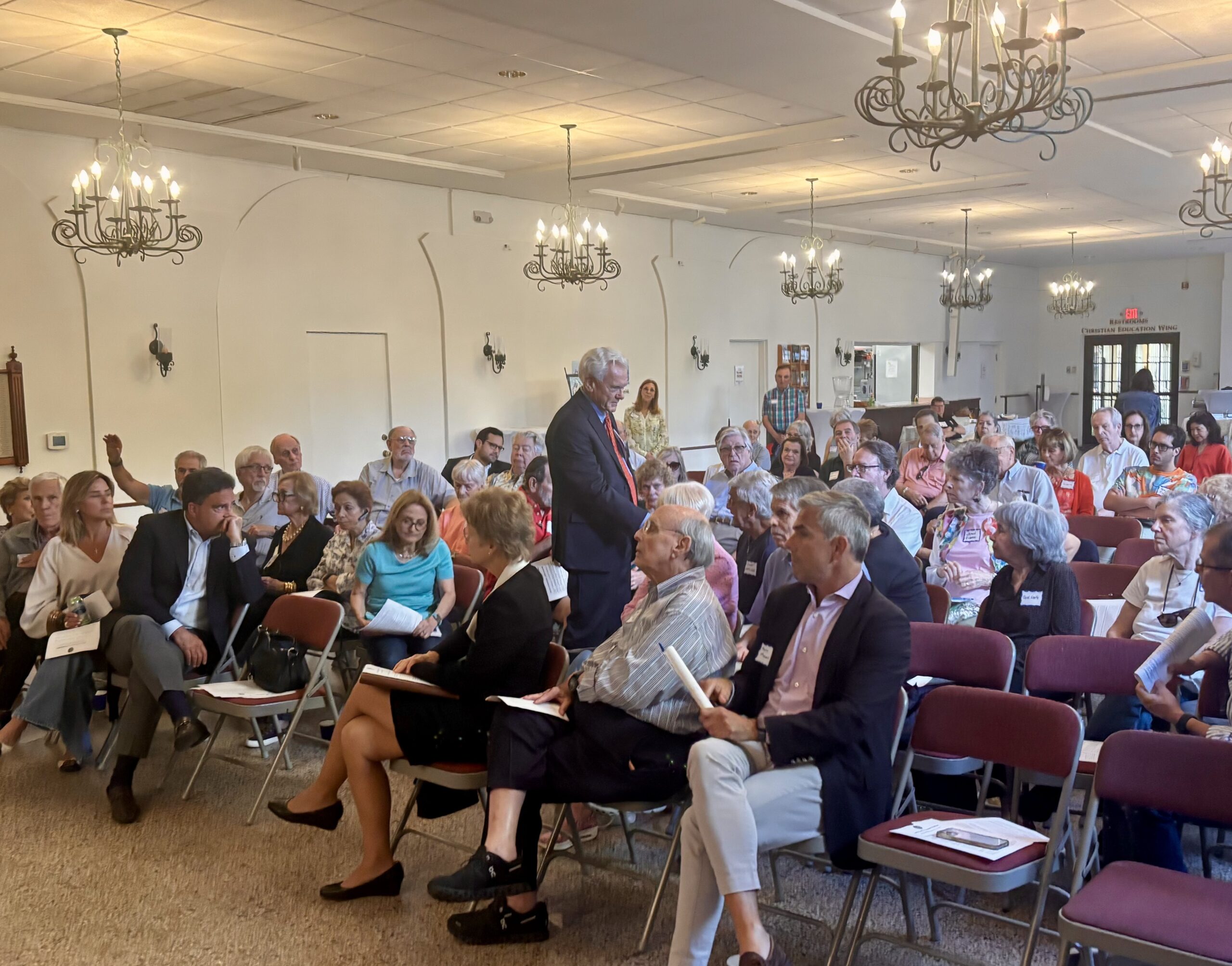 Michael Maxwell walks among seated attendees with a microphone during a community meeting in Coral Gables.