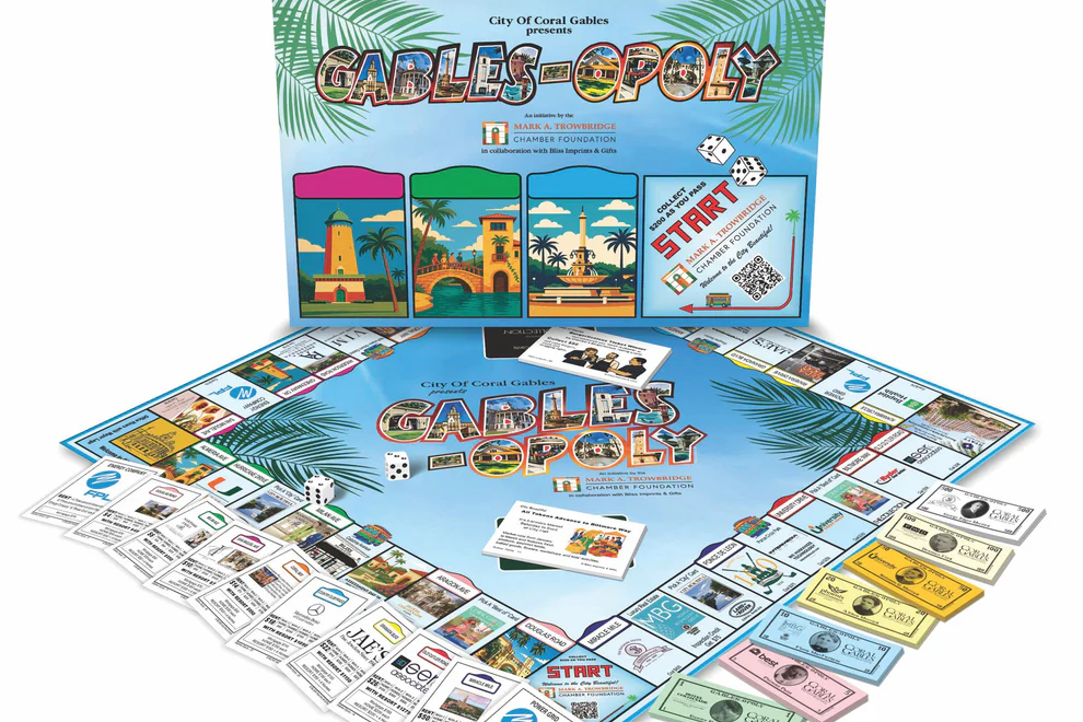 A Coral Gables-themed board game titled “Gables-Opoly” displayed with its box, game board, cards, and currency, featuring local landmarks, businesses, and city-themed design elements.