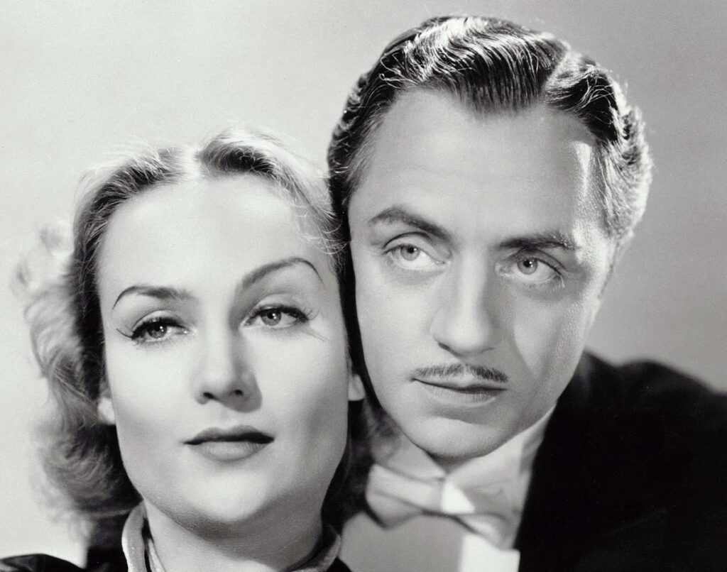 Black-and-white studio portrait of actors Carole Lombard and William Powell posed closely together, Lombard facing the camera while Powell looks slightly to the side, wearing formal attire.