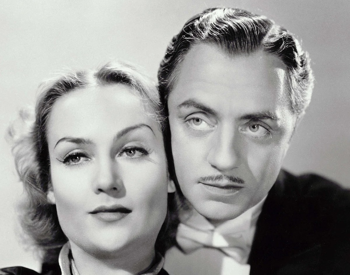 Black-and-white studio portrait of actors Carole Lombard and William Powell posed closely together, Lombard facing the camera while Powell looks slightly to the side, wearing formal attire.
