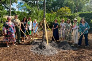 Group of people using shovels to plant a tree at a park surrounded by native vegetation during an Arbor Day event in Coral Gables.