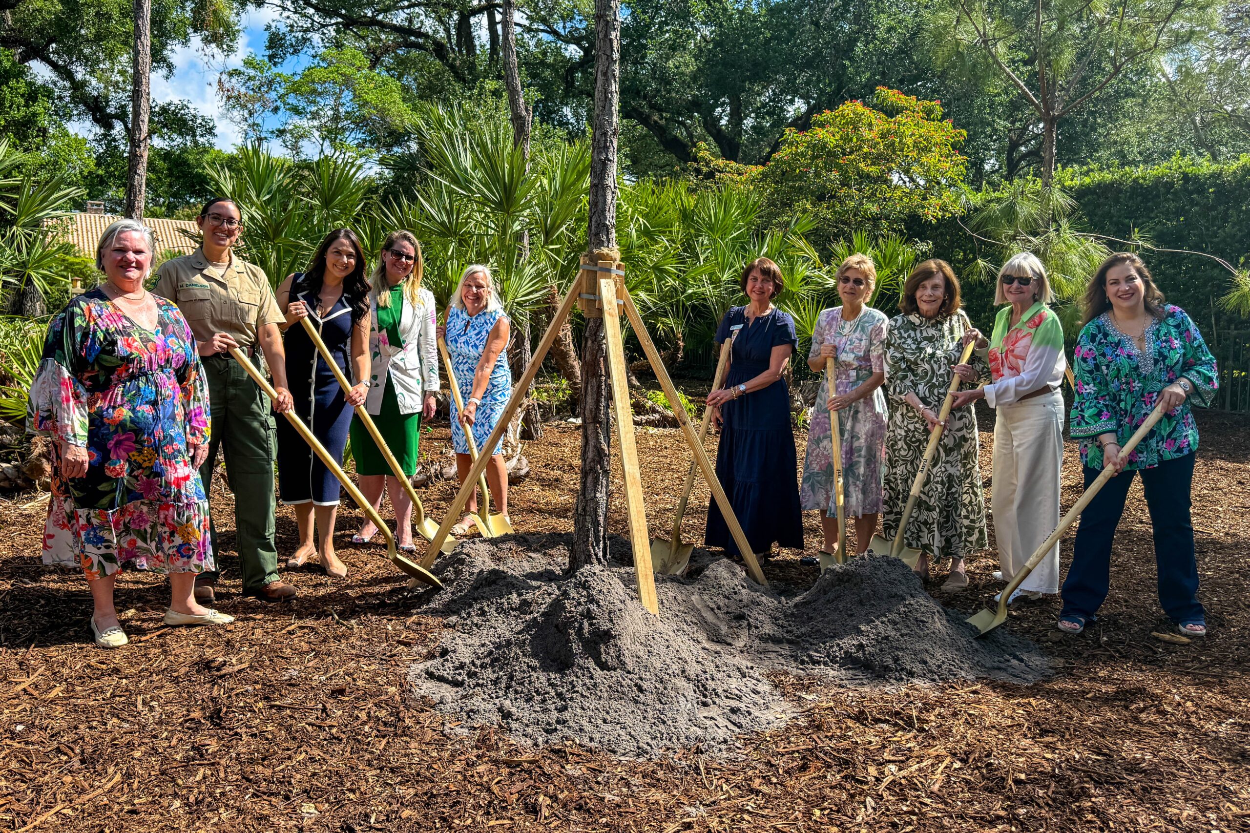 Group of people using shovels to plant a tree at a park surrounded by native vegetation during an Arbor Day event in Coral Gables.