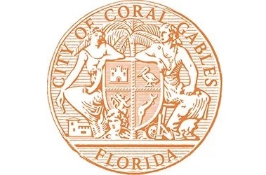 The circular official seal of the City of Coral Gables, Florida, rendered in coral orange on white. The seal depicts two classical figures flanking a shield, with a royal palm at center and the words "City of Coral Gables" and "Florida" around the perimeter.