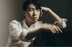 Portrait of South Korean pianist Saehyun Kim seated in a white shirt against a dark background.
