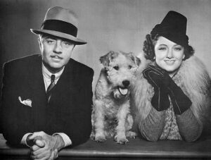 Publicity portrait from The Thin Man featuring actors William Powell and Myrna Loy posed beside Asta the wire-haired fox terrier.