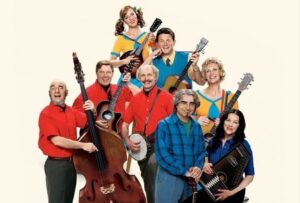 Promotional image for A Mighty Wind featuring Catherine O’Hara, Eugene Levy, Christopher Guest, Michael McKean, Harry Shearer, and other cast members holding folk instruments against a light background.