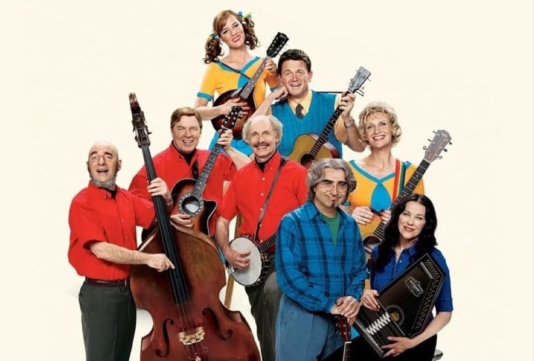 Promotional image for A Mighty Wind featuring Catherine O’Hara, Eugene Levy, Christopher Guest, Michael McKean, Harry Shearer, and other cast members holding folk instruments against a light background.