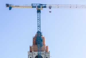 A tall construction crane stands over a partially covered building under renovation against a clear sky.
