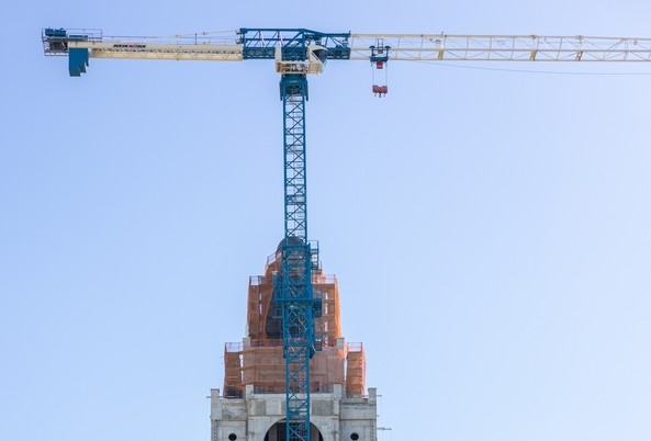 A tall construction crane stands over a partially covered building under renovation against a clear sky.