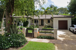 Street view of a single-story Coral Gables home at 722 Aledo Avenue with a front gate, driveway, garage and surrounding trees.