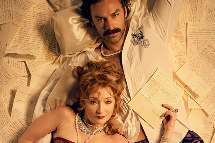 Two costumed performers recline on a bed surrounded by handwritten letters in a promotional image for Les Liaisons Dangereuses.