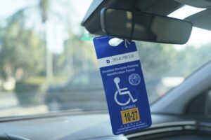 Close-up view of a blue Florida disabled parking permit hanging from a car’s rearview mirror inside a parked vehicle.