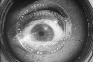 Black-and-white close-up of a human eye superimposed inside a camera lens.