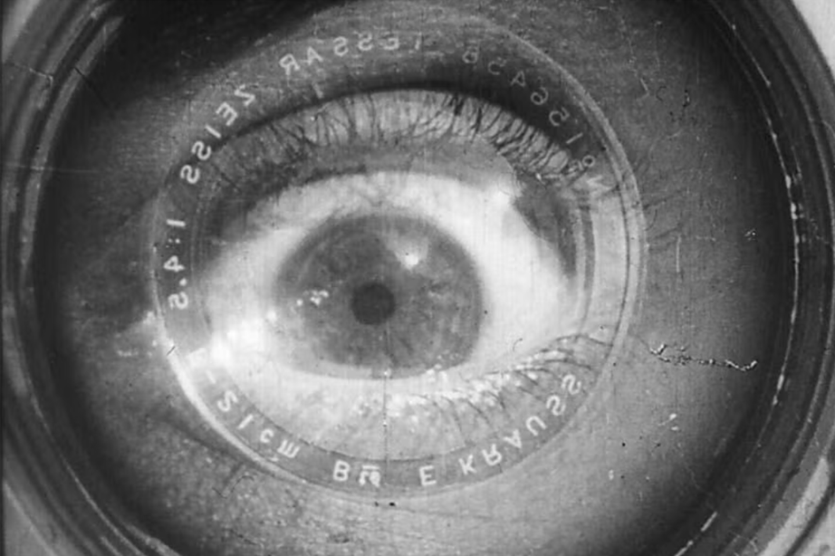 Black-and-white close-up of a human eye superimposed inside a camera lens.