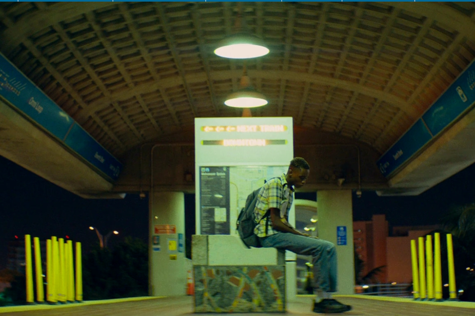 A young man sits alone on a concrete bench at night beneath the arched roof of a transit station.
