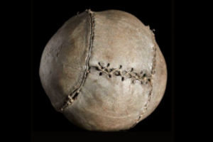Close-up photo of an aged stitched leather football against a black background.