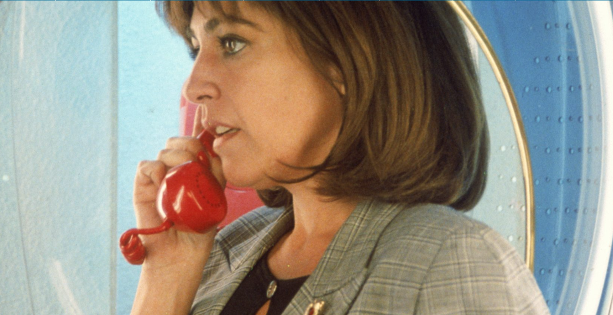 A woman holds a red telephone receiver while standing against a blue-toned background in a film still from Women on the Verge of a Nervous Breakdown.