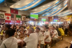 Crowded sports bar with fans, flags and television screens showing a soccer match during a World Cup viewing party.