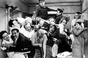 Black-and-white film still showing a crowded ship stateroom packed with people, luggage and performers in a comic pileup.