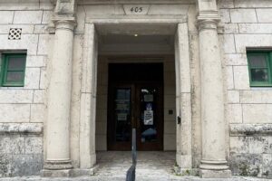 Main entrance of Coral Gables City Hall with stone columns, green-framed windows and dark wood double doors beneath the number 405.