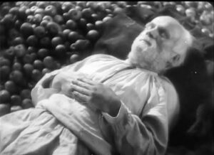 Black-and-white film still from Earth showing an older man lying beside a pile of apples.