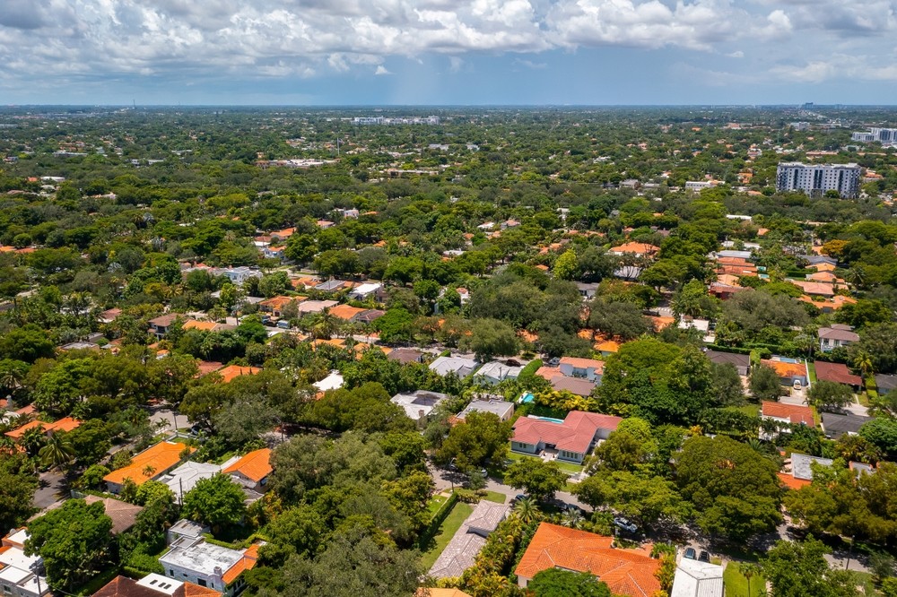 Aerial view of a tree-lined Coral Gables neighborhood with single-family homes, red-tile roofs and dense greenery stretching toward the horizon.