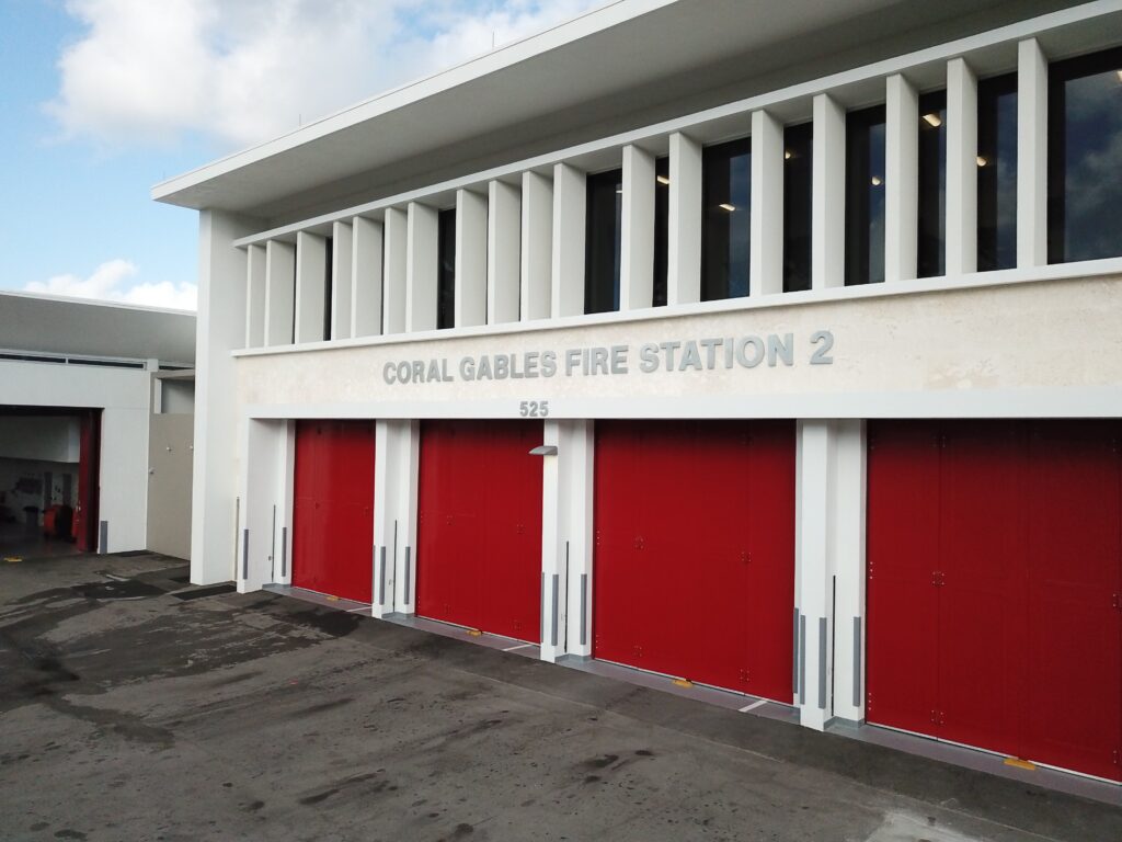 Exterior of Coral Gables Fire Station 2, showing the station’s white façade and four large red apparatus-bay doors beneath the address 525.