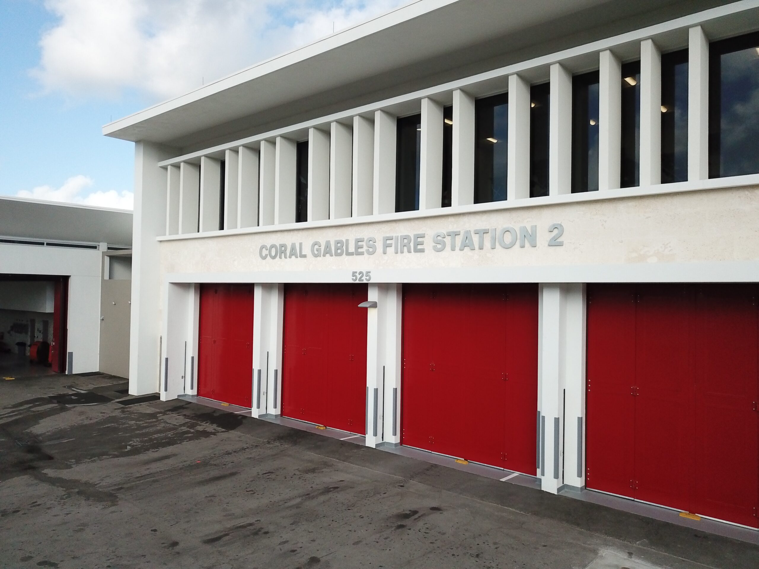 Exterior of Coral Gables Fire Station 2, showing the station’s white façade and four large red apparatus-bay doors beneath the address 525.