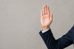 Illustration of a person in a dark suit raising a hand with the palm forward as if taking an oath.