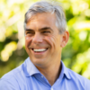 Portrait of Nestor Menendez smiling outdoors in a light blue collared shirt with trees blurred in the background.