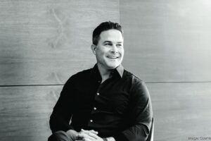 Black-and-white portrait of real estate developer Alberto J. Perez seated indoors and smiling while looking to his left.