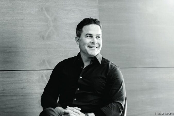 Black-and-white portrait of real estate developer Alberto J. Perez seated indoors and smiling while looking to his left.