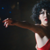 Sundance award winner about grief and ballroom dance opens at Gables Cinema Woman in a red ballroom dress extends her arm toward a dance partner in a dark scene from Ha-Chan, Shake Your Booty!.