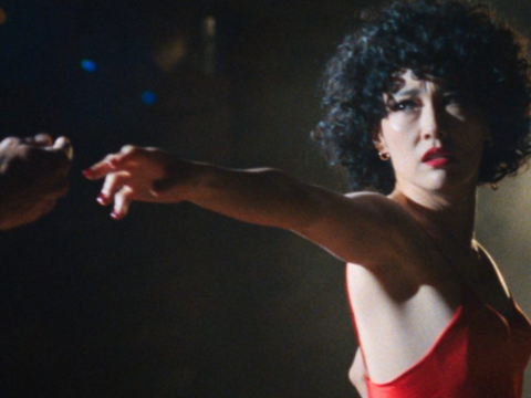 Woman in a red ballroom dress extends her arm toward a dance partner in a dark scene from Ha-Chan, Shake Your Booty!.