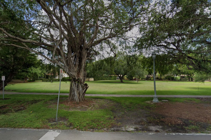 View of the grassy city-owned property at 440 University Drive in Coral Gables, with mature trees, a sidewalk and a streetlight.