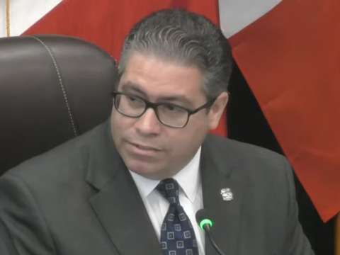 oral Gables Commissioner Ariel Fernandez, wearing glasses and a dark suit, sits at the commission dais beside a microphone during his final meeting Oct. 27, 2026.