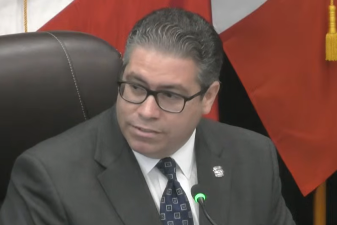 oral Gables Commissioner Ariel Fernandez, wearing glasses and a dark suit, sits at the commission dais beside a microphone during his final meeting Oct. 27, 2026.
