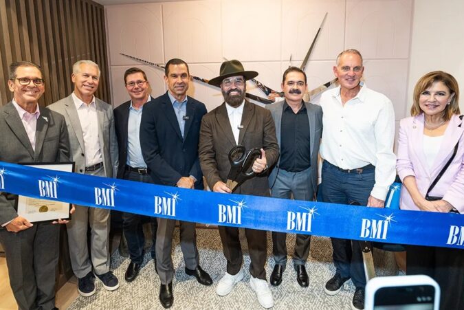 Eight executives and civic leaders stand behind a blue BMI ribbon at the opening of the music licensing company's Coral Gables office. A man in a black hat at the center holds ceremonial scissors.