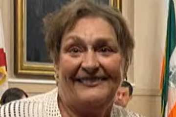 llen Uguccioni smiles inside the Coral Gables City Hall Commission Chambers, with framed artwork and flags visible behind her.