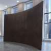 Richard Serra's Fin, a large, dark, curved steel wall with a sloping upper edge, displayed in a stone-floored Manhattan office lobby with floor-to-ceiling windows.