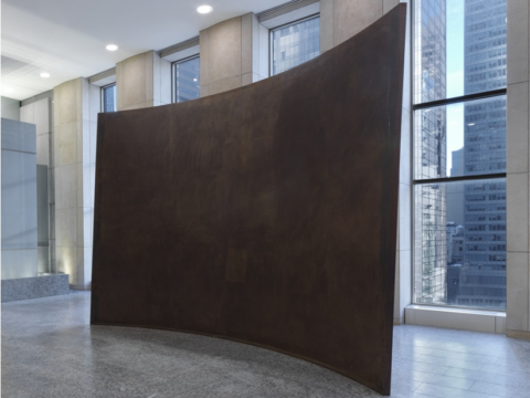 Richard Serra's Fin, a large, dark, curved steel wall with a sloping upper edge, displayed in a stone-floored Manhattan office lobby with floor-to-ceiling windows.